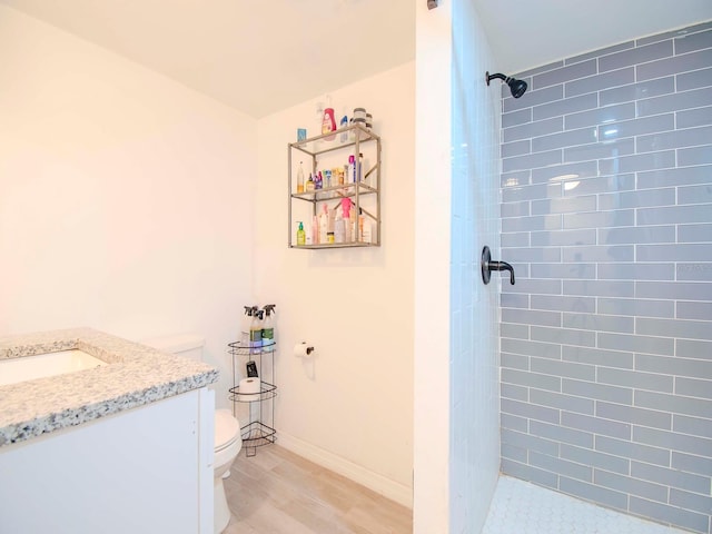 bathroom with tiled shower, wood-type flooring, vanity, and toilet