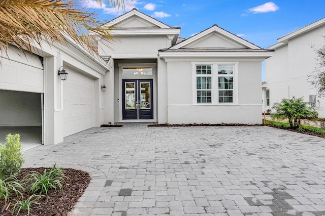 view of exterior entry with a garage, french doors, decorative driveway, and stucco siding