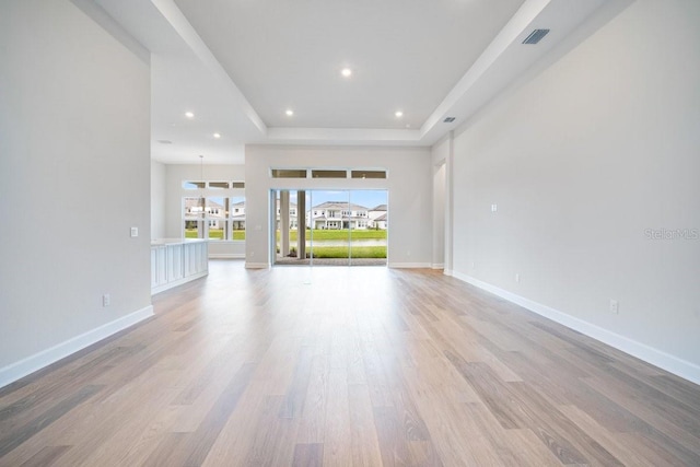 unfurnished living room with a tray ceiling, light wood-type flooring, recessed lighting, and baseboards