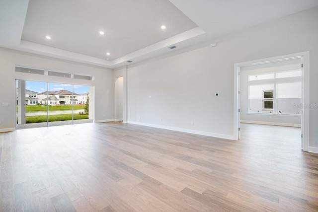 empty room with light wood-style floors, a raised ceiling, and baseboards