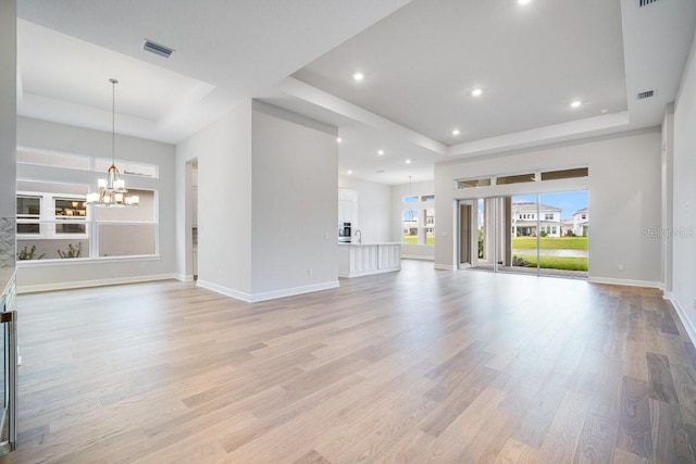 unfurnished living room featuring a chandelier, a tray ceiling, and light wood-style flooring