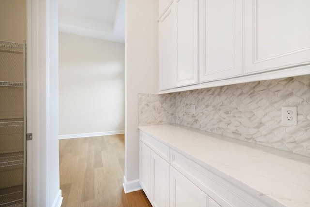 interior space featuring tasteful backsplash, baseboards, light wood-style flooring, light stone counters, and white cabinetry