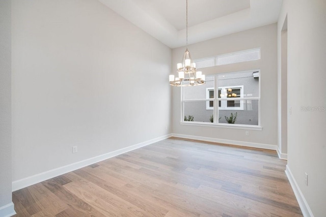 empty room with an inviting chandelier, baseboards, and wood finished floors