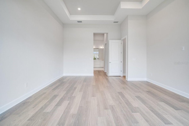 spare room featuring light wood finished floors, visible vents, baseboards, and a raised ceiling