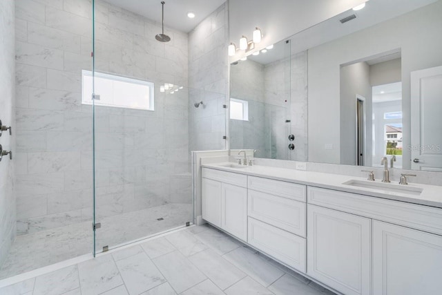 bathroom with marble finish floor, tiled shower, a sink, and visible vents