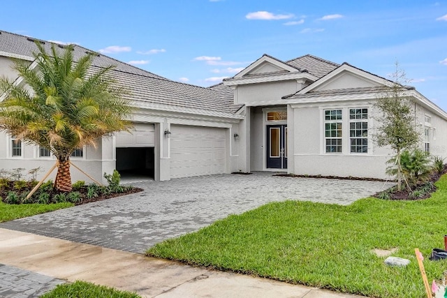 ranch-style home with a front yard, decorative driveway, an attached garage, and stucco siding