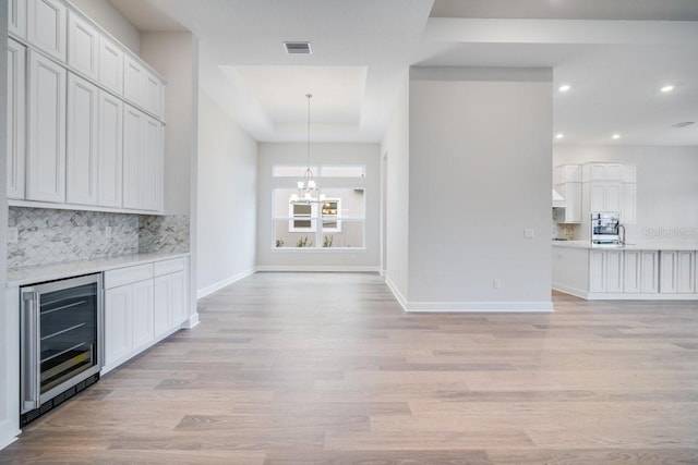 unfurnished living room featuring baseboards, visible vents, light wood finished floors, wine cooler, and a chandelier