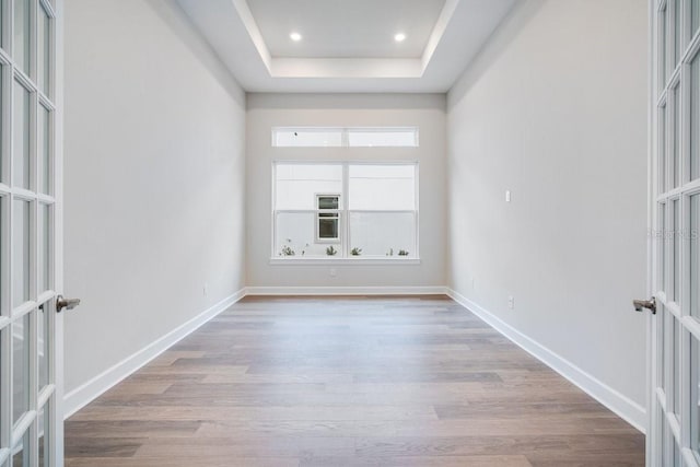 unfurnished room with light wood finished floors, french doors, a raised ceiling, and baseboards