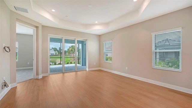 unfurnished room featuring a tray ceiling and light hardwood / wood-style flooring