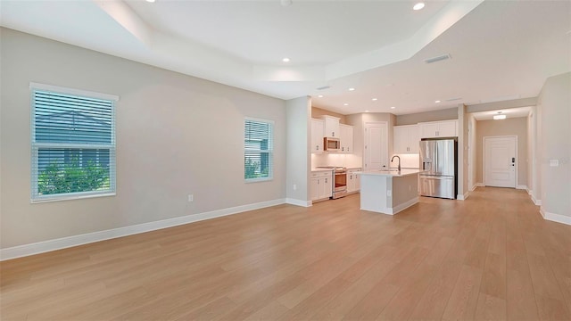 unfurnished living room featuring a raised ceiling, sink, and light hardwood / wood-style flooring