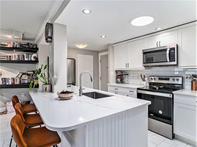 kitchen featuring a kitchen breakfast bar, light tile flooring, backsplash, white cabinets, and appliances with stainless steel finishes