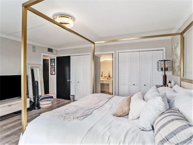 bedroom with two closets, wood-type flooring, ornamental molding, and a textured ceiling