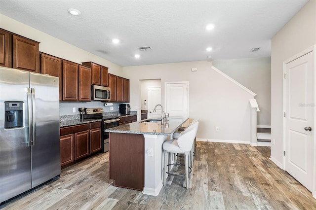 kitchen featuring a kitchen bar, light hardwood / wood-style floors, appliances with stainless steel finishes, a kitchen island with sink, and sink