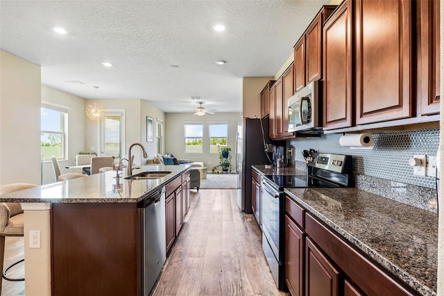 kitchen featuring a breakfast bar area, stainless steel appliances, hanging light fixtures, light hardwood / wood-style flooring, and sink