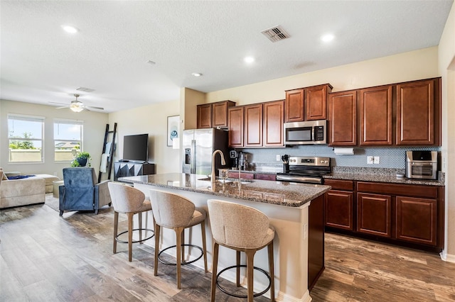 kitchen with hardwood / wood-style floors, an island with sink, stainless steel appliances, a breakfast bar, and sink