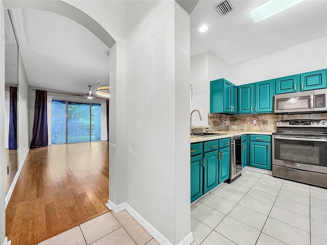 kitchen featuring appliances with stainless steel finishes, backsplash, light hardwood / wood-style floors, ceiling fan, and wine cooler