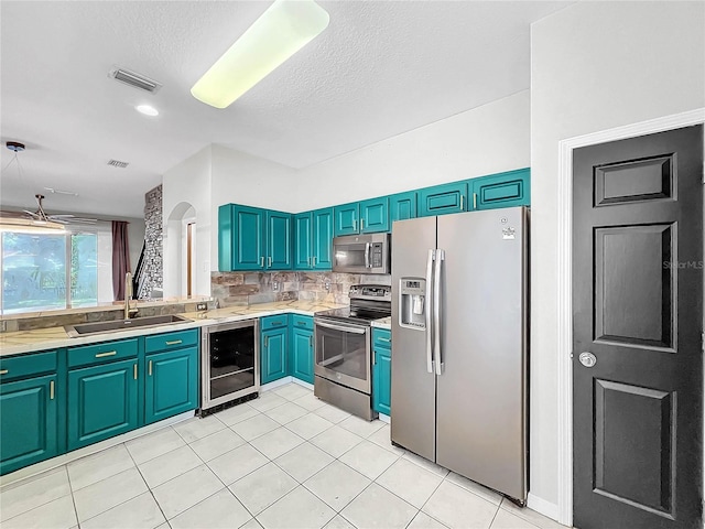 kitchen featuring sink, light tile patterned flooring, a textured ceiling, stainless steel appliances, and beverage cooler