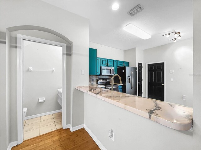 kitchen with blue cabinetry, hardwood / wood-style floors, stainless steel appliances, and tasteful backsplash