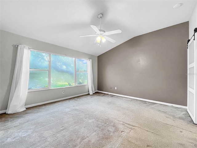 carpeted spare room featuring ceiling fan, vaulted ceiling, and a barn door