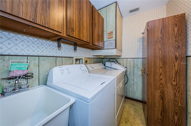 laundry room with cabinet space, wallpapered walls, a textured ceiling, washing machine and dryer, and a sink