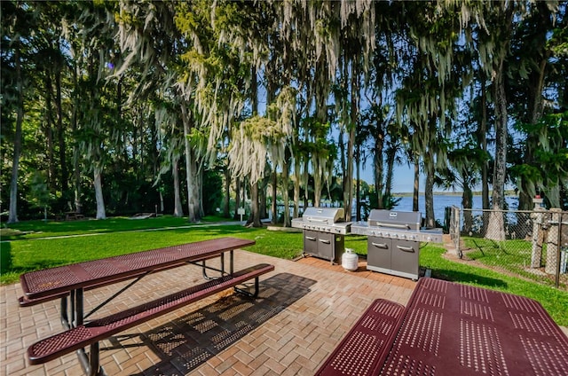 surrounding community featuring a water view, a patio area, fence, and a lawn