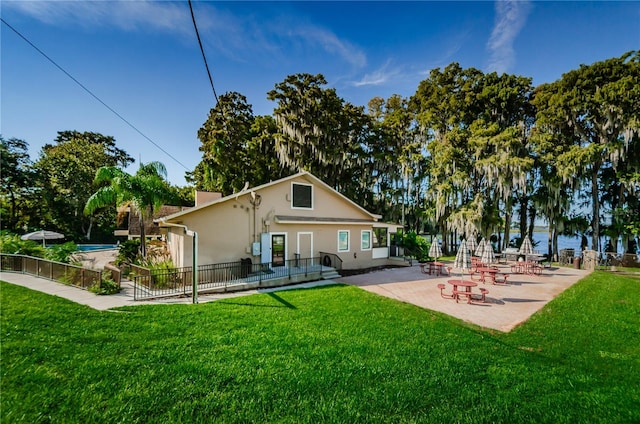 rear view of property with a water view, fence, a lawn, and a patio