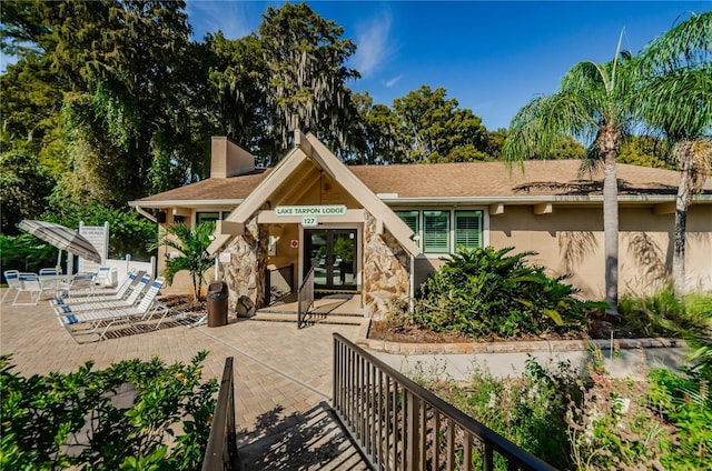 exterior space with french doors, a patio, a chimney, stucco siding, and stone siding