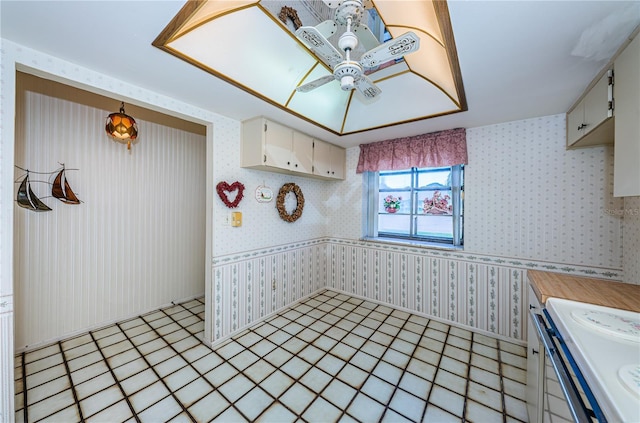 kitchen with wallpapered walls, light tile patterned floors, a ceiling fan, light countertops, and range with electric stovetop