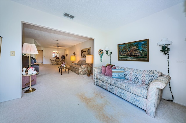 carpeted living area with a textured ceiling, ceiling fan, and visible vents