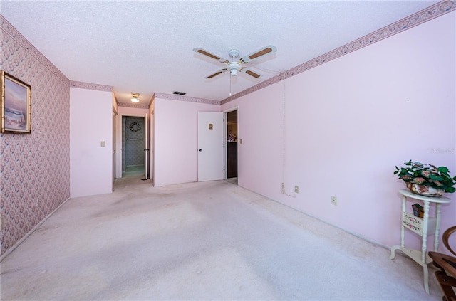 spare room featuring light carpet, wallpapered walls, visible vents, a ceiling fan, and a textured ceiling