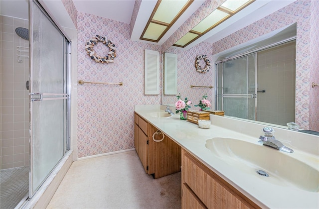 full bathroom with double vanity, tiled shower, a sink, and wallpapered walls