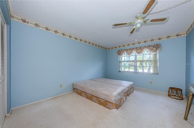 unfurnished bedroom featuring a ceiling fan, carpet, baseboards, and a textured ceiling