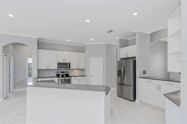 kitchen featuring appliances with stainless steel finishes, backsplash, a kitchen island with sink, crown molding, and white cabinets