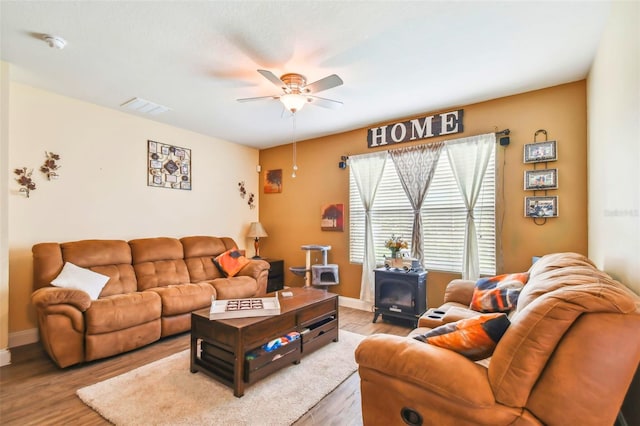 living room with ceiling fan, a wood stove, and hardwood / wood-style floors