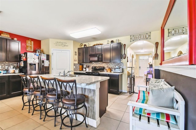 kitchen with a center island with sink, black appliances, a breakfast bar, light tile patterned flooring, and sink