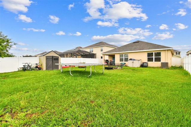 rear view of property with central AC unit, a trampoline, a storage unit, and a yard