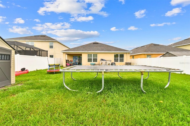 rear view of property featuring a trampoline and a yard