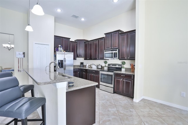 kitchen with light stone countertops, decorative light fixtures, light tile flooring, a breakfast bar, and appliances with stainless steel finishes