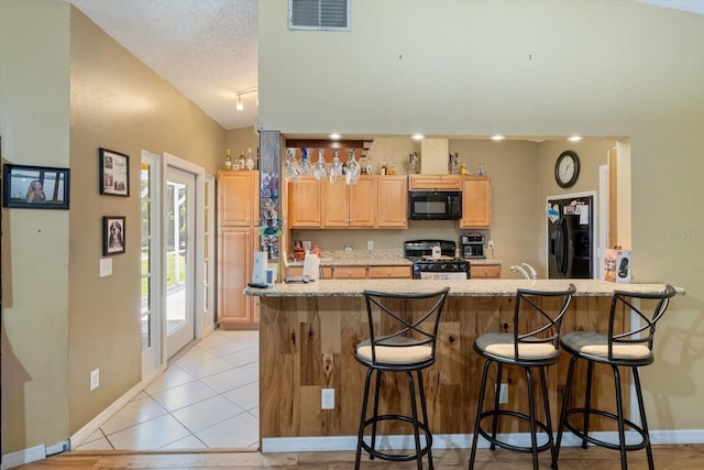 kitchen with vaulted ceiling, light stone counters, black appliances, light tile floors, and a breakfast bar