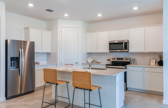 kitchen with sink, appliances with stainless steel finishes, a kitchen island with sink, tasteful backsplash, and white cabinetry