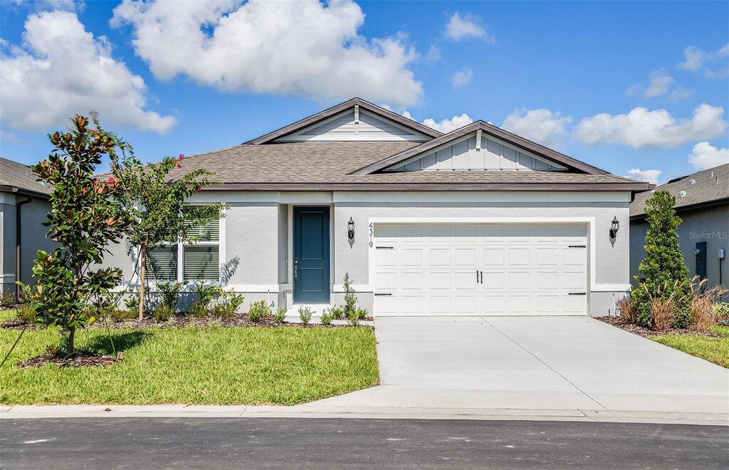 ranch-style home with a shingled roof, concrete driveway, an attached garage, a front lawn, and stucco siding