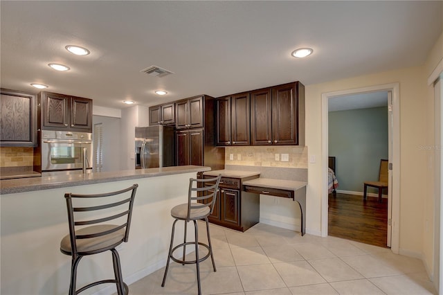 kitchen with dark brown cabinetry, a breakfast bar area, tasteful backsplash, light tile patterned floors, and stainless steel appliances