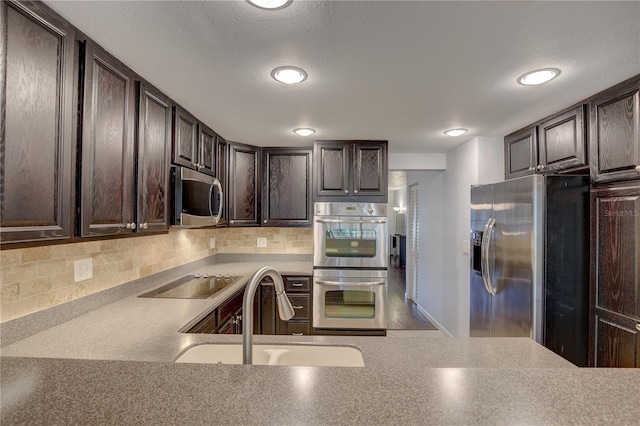 kitchen with stainless steel appliances, dark brown cabinets, sink, and backsplash