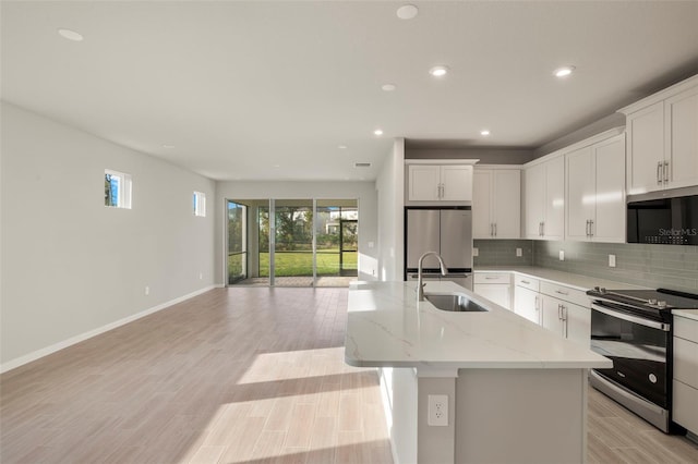 kitchen with a center island with sink, light stone countertops, sink, and appliances with stainless steel finishes