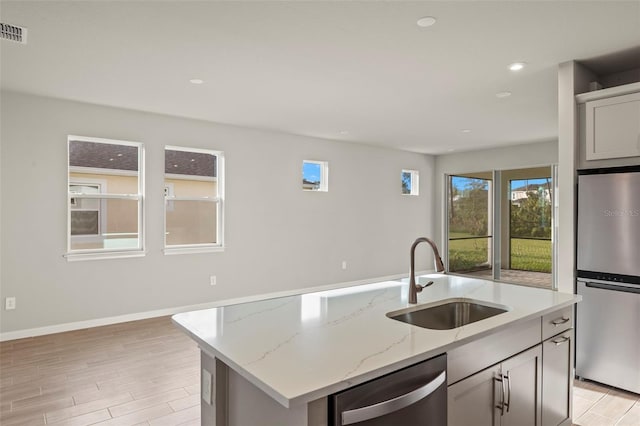 kitchen featuring light stone counters, stainless steel appliances, sink, light hardwood / wood-style floors, and an island with sink