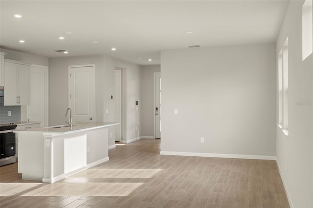 kitchen with a kitchen island with sink, white cabinets, sink, stainless steel stove, and decorative backsplash