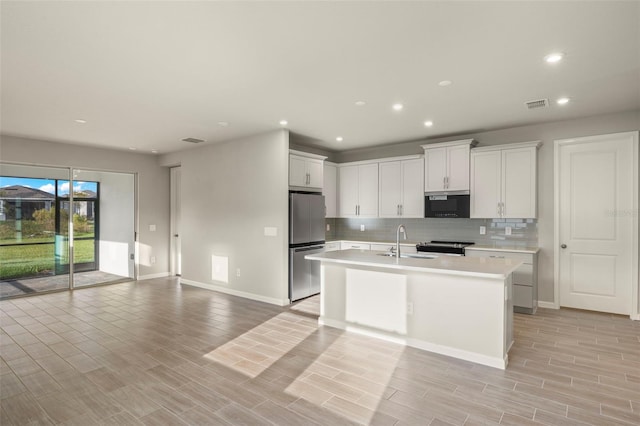 kitchen with white cabinetry, sink, a kitchen island with sink, decorative backsplash, and appliances with stainless steel finishes