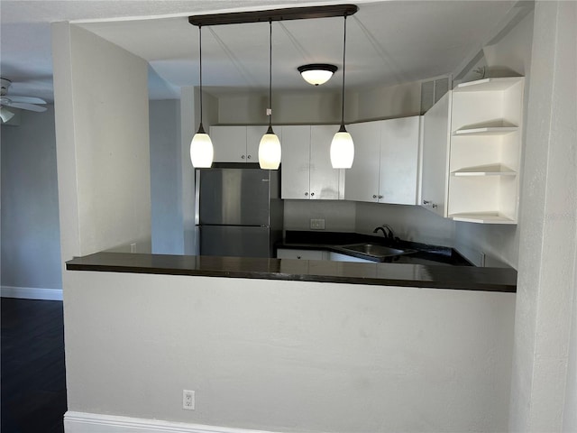 kitchen featuring stainless steel refrigerator, ceiling fan, sink, hanging light fixtures, and white cabinets