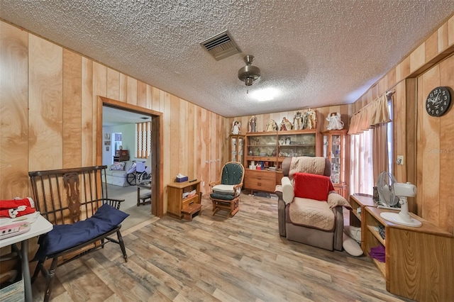 living area with hardwood / wood-style floors, wooden walls, and a textured ceiling