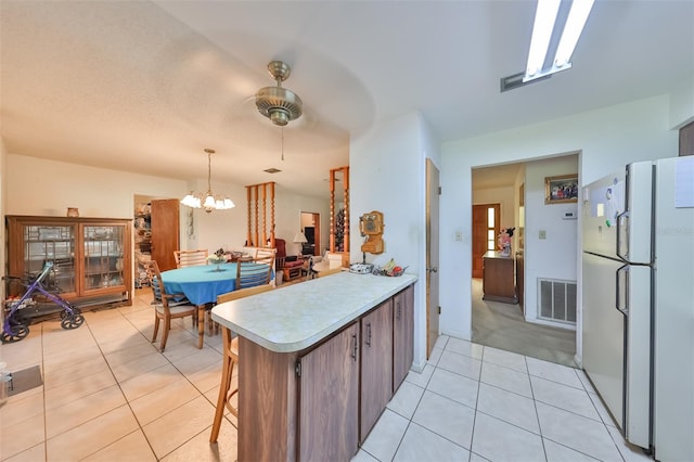 kitchen with ceiling fan with notable chandelier, a breakfast bar, kitchen peninsula, and white fridge